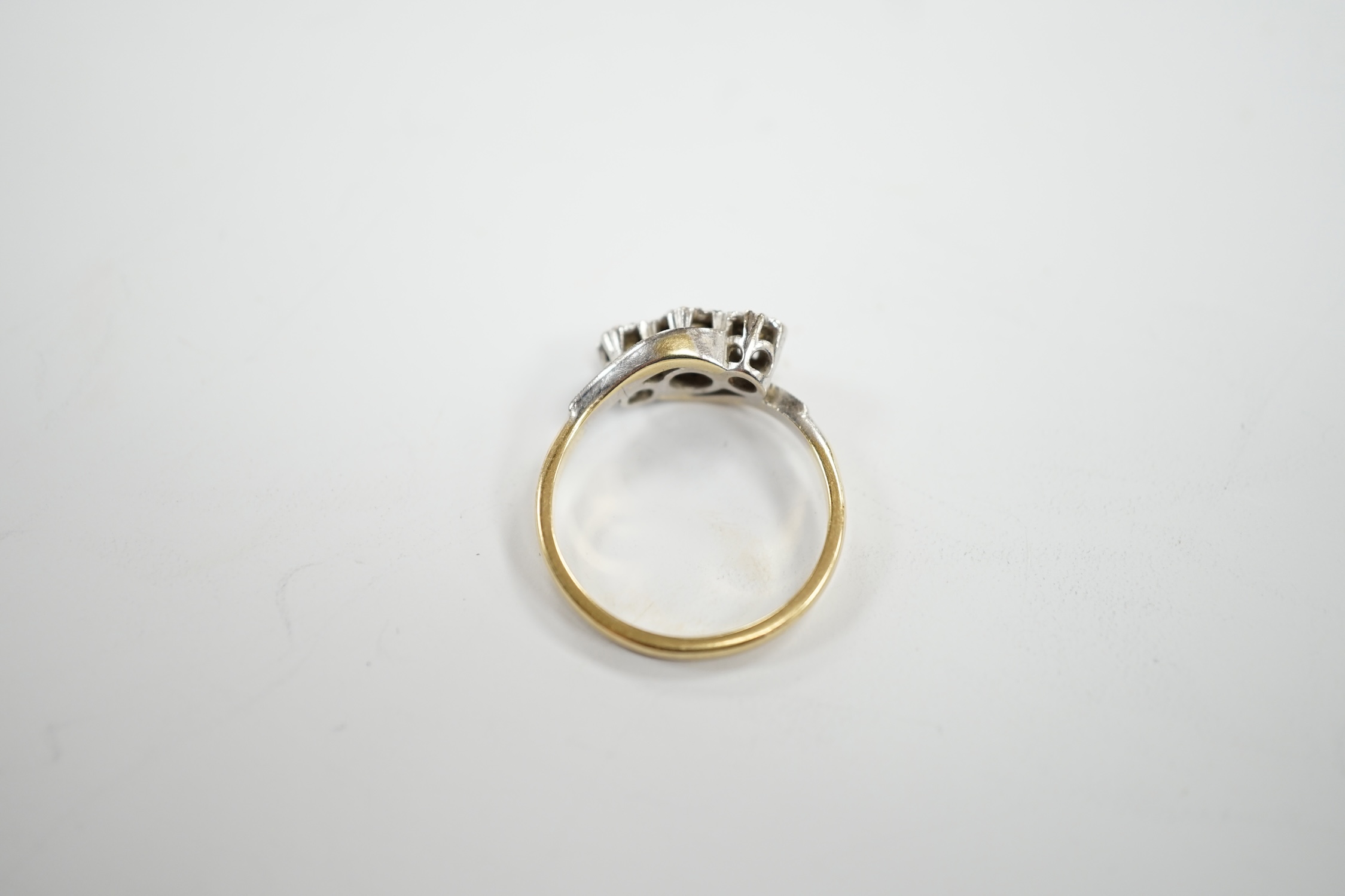 A mid to late 20th century 18ct gold and illusion set three stone diamond crossover ring, size N, gross weight 3.3 grams.